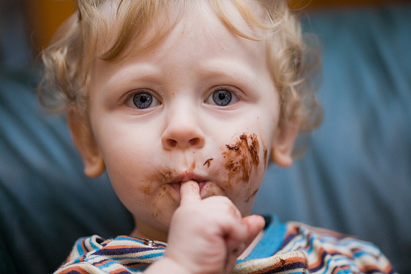 einjhriger Junge lutscht sich die Schokoladenfinger ab